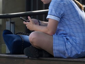 FILE - A young girl uses her phone while sitting on a bench in Sydney, Nov. 8, 2024.