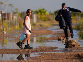FILE -- A young girl carrying an empty water bottle through a flooded street caused by an overflowing water reservoir in Hammanskraal, Pretoria, South Africa, May 26, 2023 during a cholera outbreak.