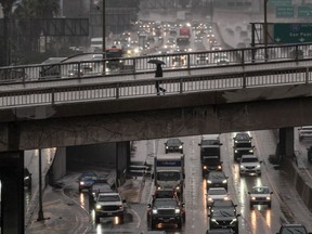A pedestrian with an umbrella walks on a bridge over the rain-soaked 110 Freeway in Los Angeles Friday, Nov. 14, 2025.