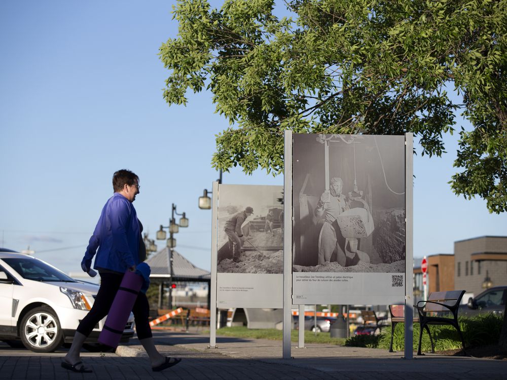 A pedestrian passes historic photographs of an aluminum factory in the town of Arvida in Saguenay, Que.
