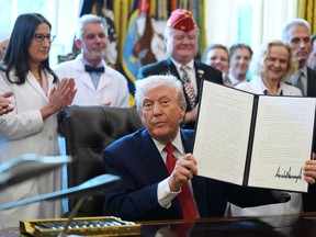 President Donald Trump displays an executive order reclassifying marijuana as a less dangerous drug in the Oval Office of the White House, Thursday, Dec. 18, 2025, in Washington.