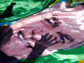 The shadow of a supporter of former President Jair Bolsonaro is cast on an image of him displayed outside the hospital where he was transported from prison for surgery the next day, in Brasilia, Brazil, Wednesday, Dec. 24, 2025.