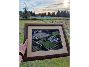 A framed photo of Dogwood Fur Farms in Aldergrove, B.C. prior to the mink farming ban is held up against the current farm, which has been decommissioned. The farm was a multigenerational business that was started in 1957. (Courtesy Angela Bernemann.)