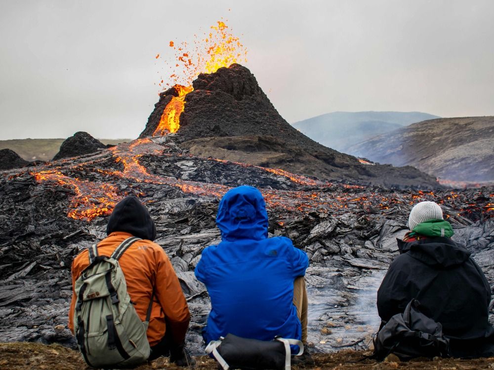 Three tourists sit before a low erupting caldera, from a safe distance