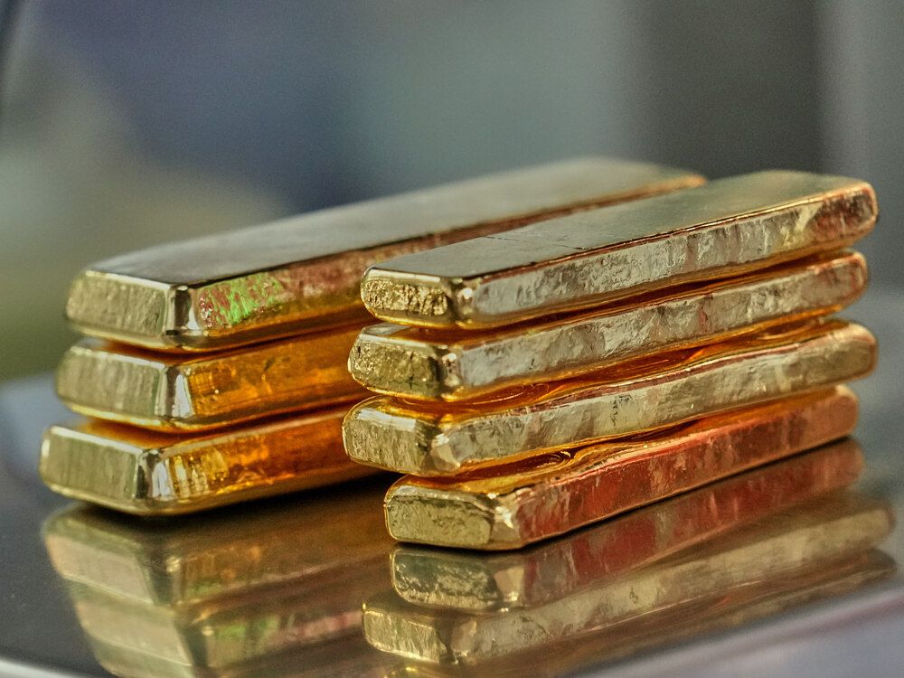 Seven thin bars of gold in two stacks on a reflective surface