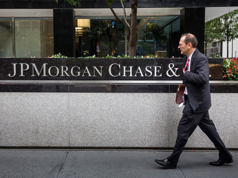 A man in a suit walks past the headquarters of JPMorgan Chase & Co, their name in silver inset into marble