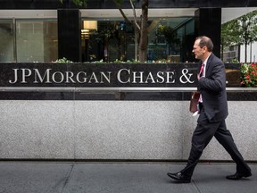 A man in a suit walks past the headquarters of JPMorgan Chase & Co, their name in silver inset into marble