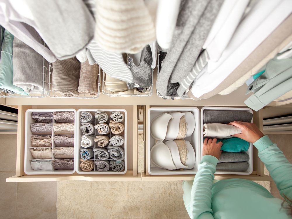 Unidentified neat housewife puts container with socks and pantyhose on wardrobe drawer during general cleaning by modern storage system.