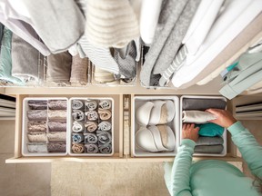 Unidentified neat housewife puts container with socks and pantyhose on wardrobe drawer during general cleaning by modern storage system.