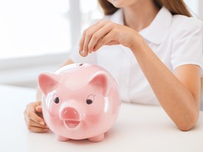 Close up of young woman putting coin into big piggy bank