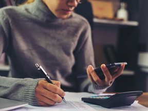 Woman in grey sweater doing taxes with a phone, calculator and tax forms.
