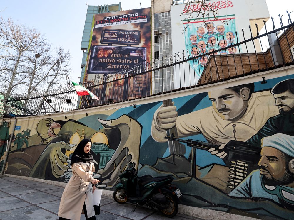 A woman walks past an anti-Israeli and anti-US billboard hanging from a building that reads in Persian 