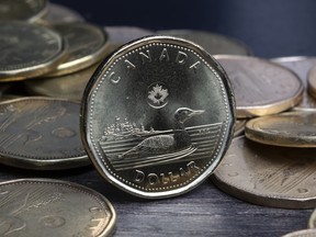 A Canadian loonie stands upright on its edge among other loonies laying on their faces