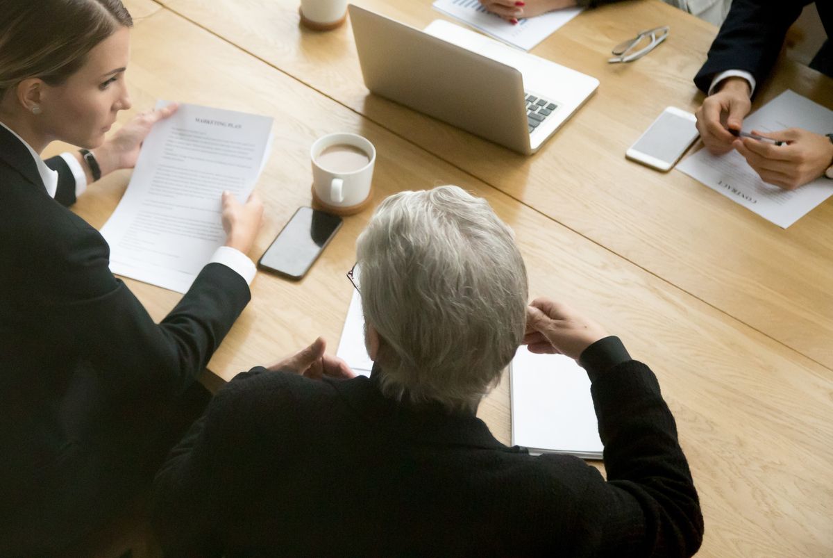 Young and senior partners team thinking talking consulting about contract sitting at conference office table.