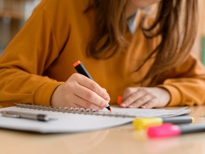 Young unrecognisable female college student in class, taking notes and using highlighter. Focused student in classroom. Authentic Education concept.