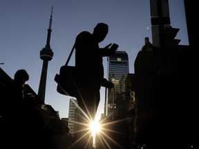 A pedestrian uses his cell phone on Bay Street at Front Street as the sun sets behind the CN Tower and TD building in Toronto on October 8, 2025.