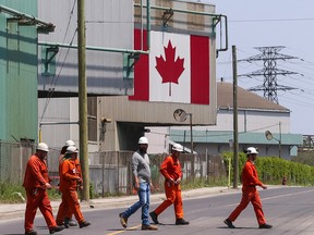 A Canadian national flag is seen in the background as workers cross the street in front of ArcelorMittal Dofasco's steel manufacturing buildings in Hamilton, Ontario, Canada, on Wednesday, June 4, 2025.