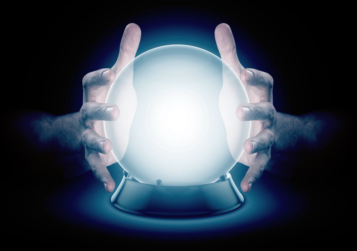 A pair of male hands surrounding a crystal ball conjuring up a hologram on an isolated dark studio background