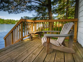 An adirondack chair sitting on a cottage wooden deck facing a calm lake during a summer day in Muskoka, Ontario Canada.