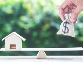 Balance home and money, home loan, reverse mortgage concept : A man hand put us dollar money bag into scales on table with green nature as background. Savings, investment, loan for plan in the future.