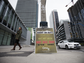 A pedestrian passes in front of a real estate sign displayed outside a residential building in Toronto, Ontario, Canada, on Thursday, May 11, 2017.