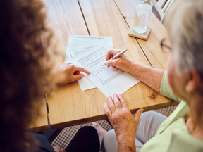 A senior aged woman signing documents with a financial adviser in her home.