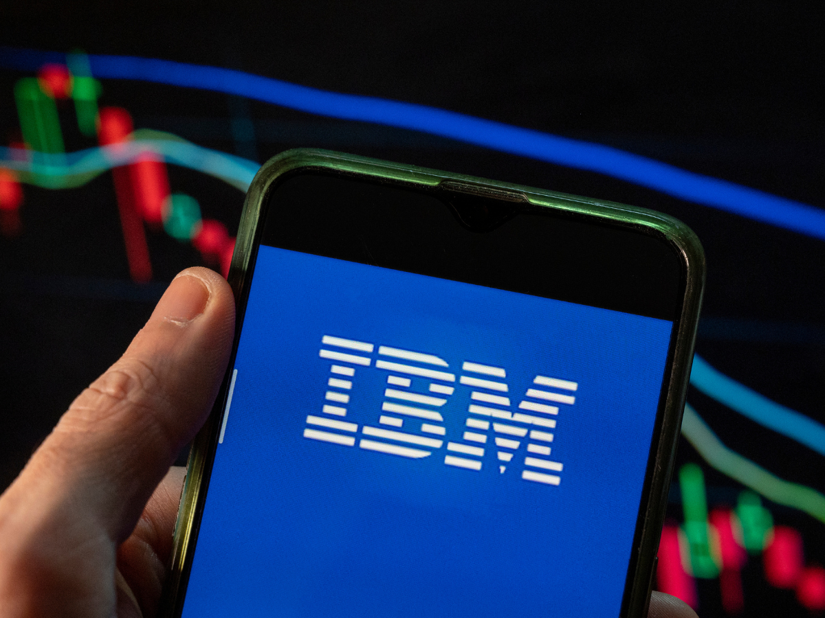 In this photo illustration the American multinational information technology company IBM logo seen displayed on a smartphone with an economic stock exchange index graph in the background.