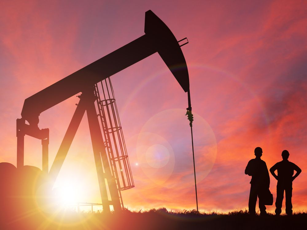 Pump jack silhouette and hard hat workers against a sunset sky with deliberate lens flare and copy space.