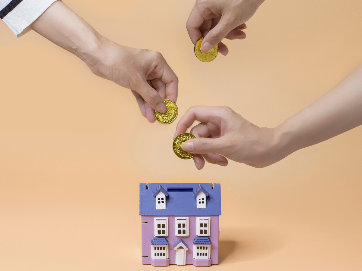 Hands inserting coin into house shape coin bank.