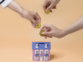 Hands inserting coin into house shape coin bank.