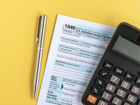 US Individual Income Tax Return Forms 1040 - stock photo on yellow background with a silver pen and calculator