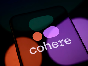 The Cohere logo is displayed on a smartphone screen placed on a reflective surface onto which the company logo is projected
