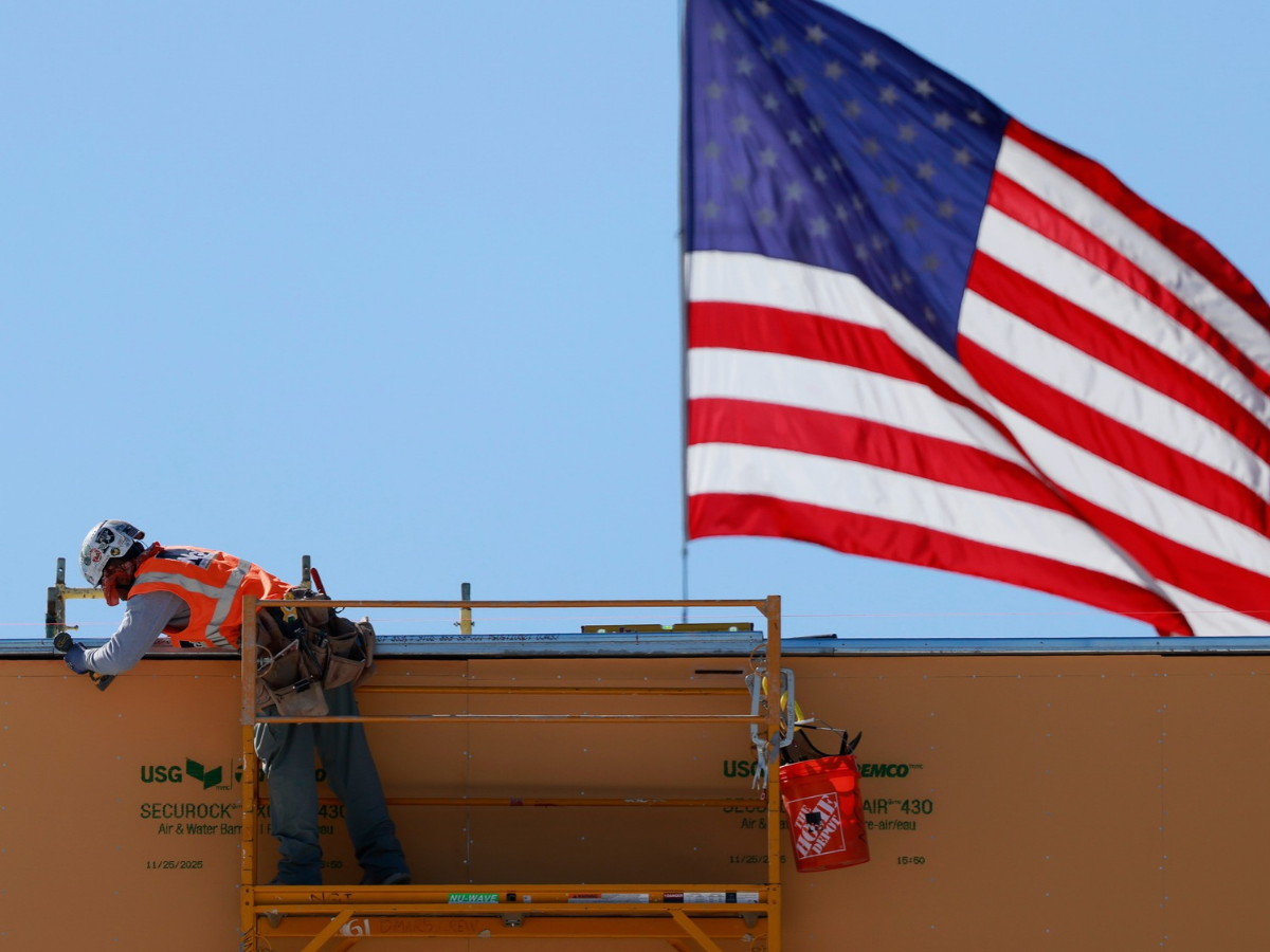An American flag flies near a construction worker during construction of a new building on March 6, 2026 in Pasadena, California