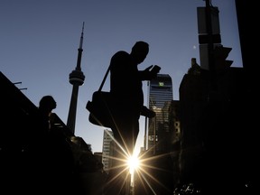 A pedestrian uses his cell phone on Bay Street at Front Street as the sun sets behind the CN Tower and TD building in Toronto, Wednesday October 8, 2025.