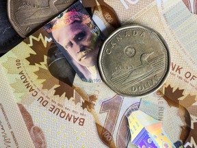 Canadian one dollar coins, also known as Loonies, and Canadian one hundred dollar banknotes are arranged for a photograph in Ontario, Canada.