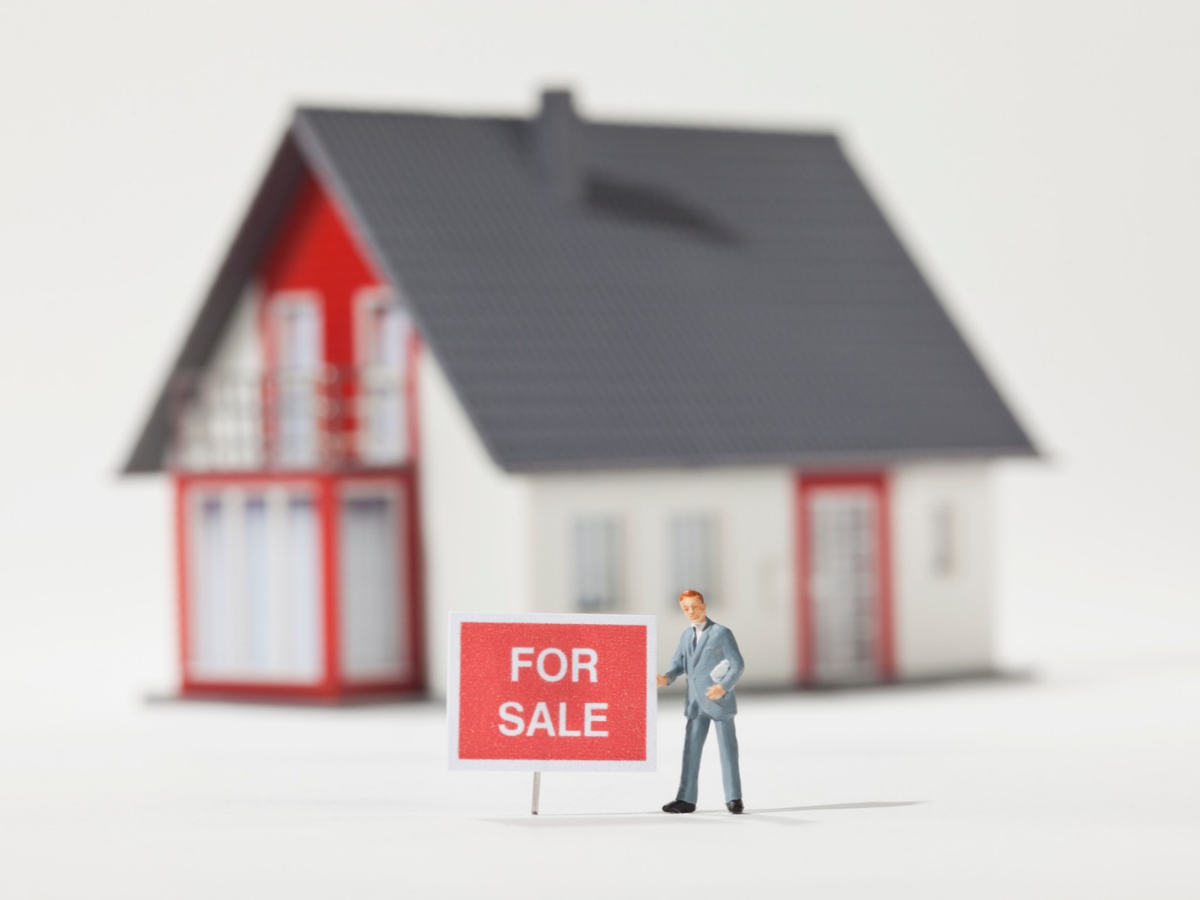A miniature real estate agent figurine standing next to a FOR SALE sign