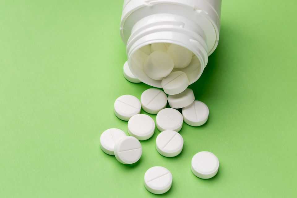 Heap of round white tablets and plastic pills bottle on green background