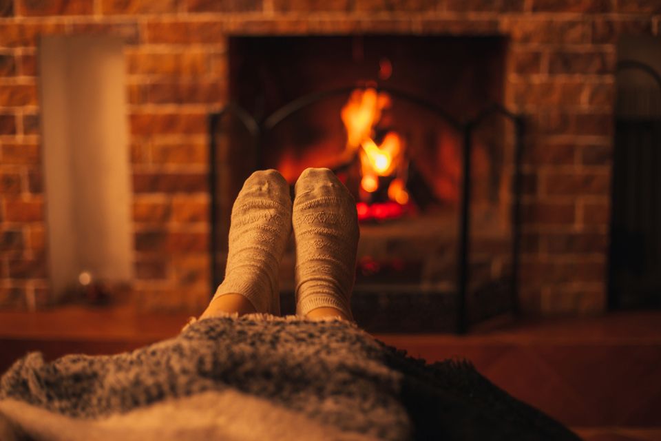 Female feet wearing white socks sitting near fireplace, wrapping in a woolen blanket.