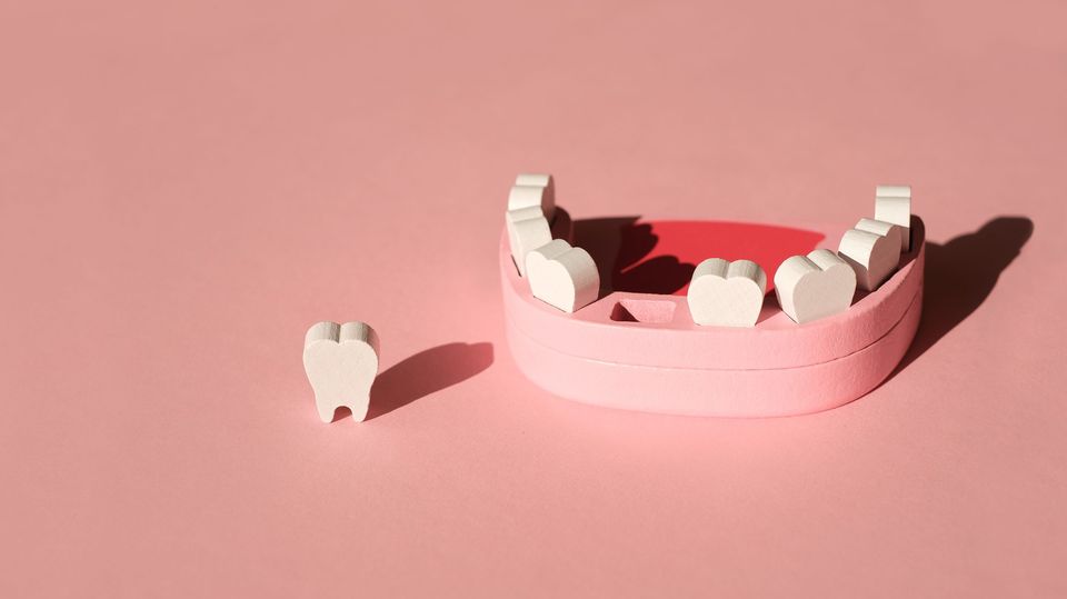 Wooden model toy of a human jaw with a missing tooth on pink background