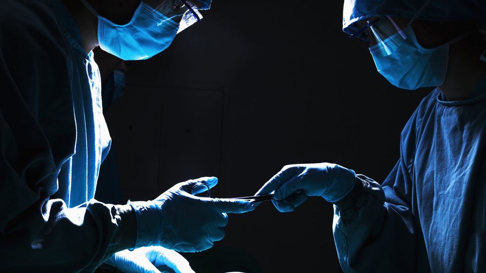 Surgeons passing surgical equipment in the operating room, dark