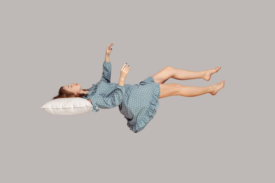 Sleeping beauty floating in air. Relaxed girl in vintage ruffle dress keeping eye closed, lying on pillow levitating