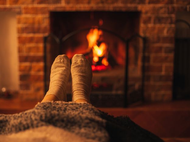 Female feet wearing white socks sitting near fireplace, wrapping in a woolen blanket.