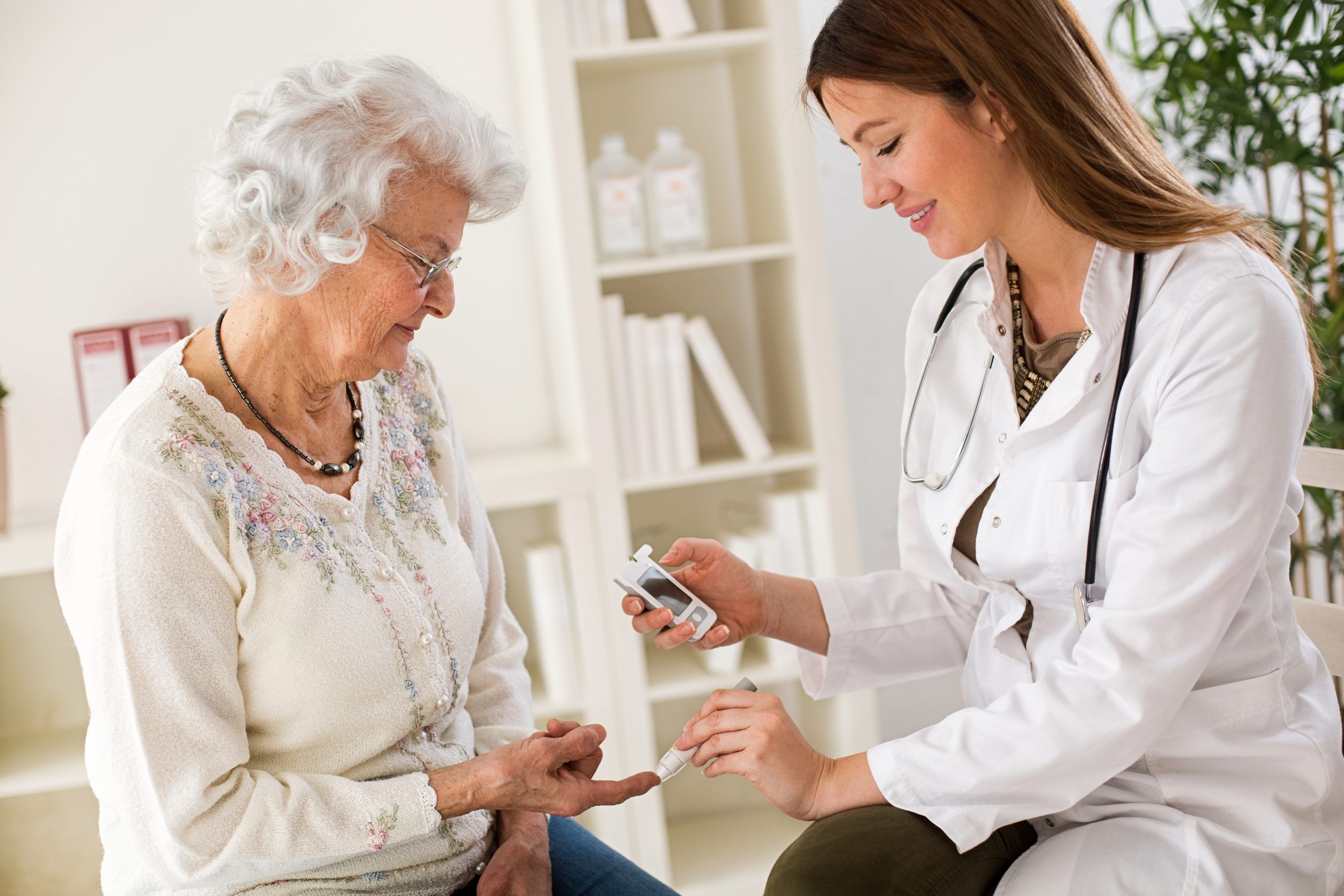 Young female doctor making diabetes blood test on senior woman