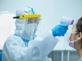 Doctor in hazmat suit and face shield taking someone's temperature