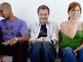 Young man, smiling, sitting between man and woman holding noses