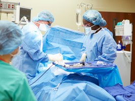 Surgical Team Working In Operating Theatre Wearing Protective Clothing