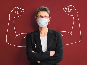 woman with mask standing against a wall with chalk outline of muscled arms