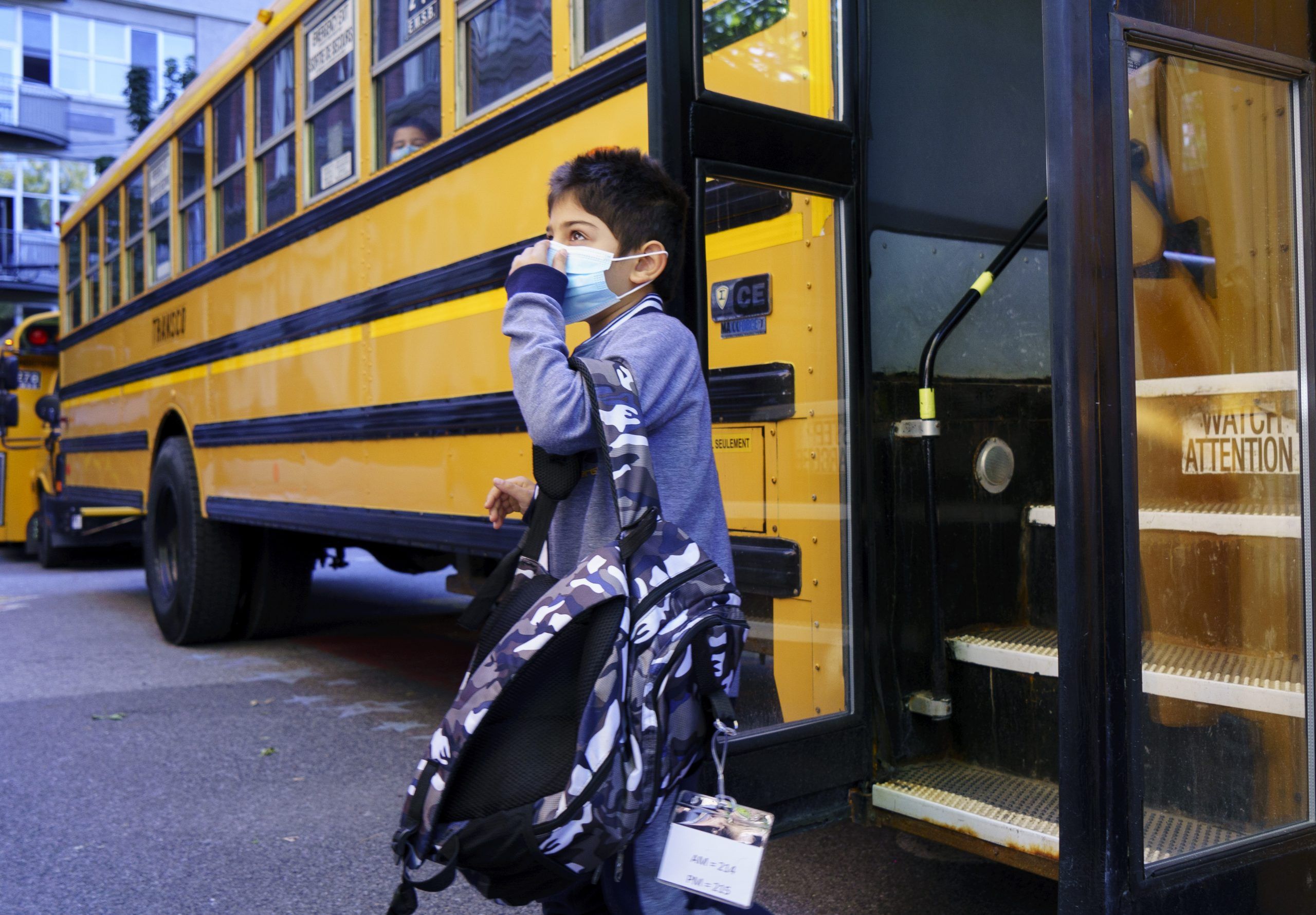 A student adjusts his protective mask as he walks off the bus at the Bancroft Elementary School as students go back to school in Montreal, on Monday, August 31, 2020.
