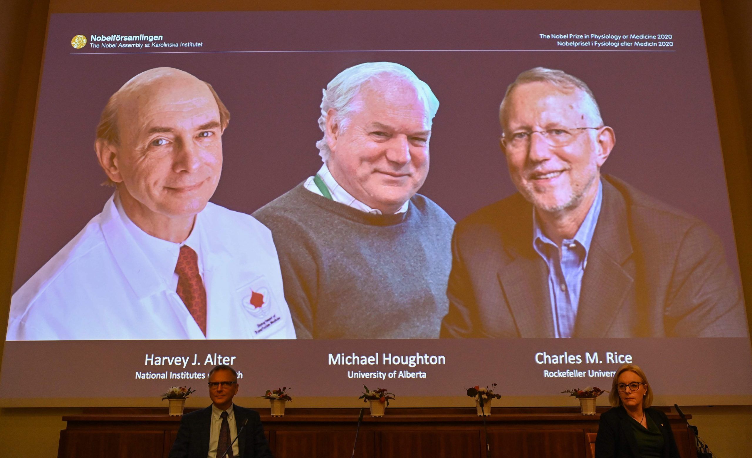 Nobel Committee members Patrik Ernfors (L) and Gunilla Karlsson Hedestam sit in front of a screen displaying the winners of the 2020 Nobel Prize in Physiology or Medicine (L-R) American Harvey Alter, Briton Michael Houghton and American Charles Rice during a press conference at the Karolinska Institute in Stockholm, Sweden, on October 5, 2020. - Americans Harvey Alter and Charles Rice together with Briton Michael Houghton won the Nobel Medicine Prize on Monday for the discovery of the Hepatitis C virus, the Nobel jury said. 