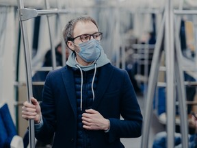 Pensive young man in eyewear wears protective surgical mask during coronavirus outbreak, poses in public transportation, thinks how to overcome disease. Virus protection, quarantine concept.